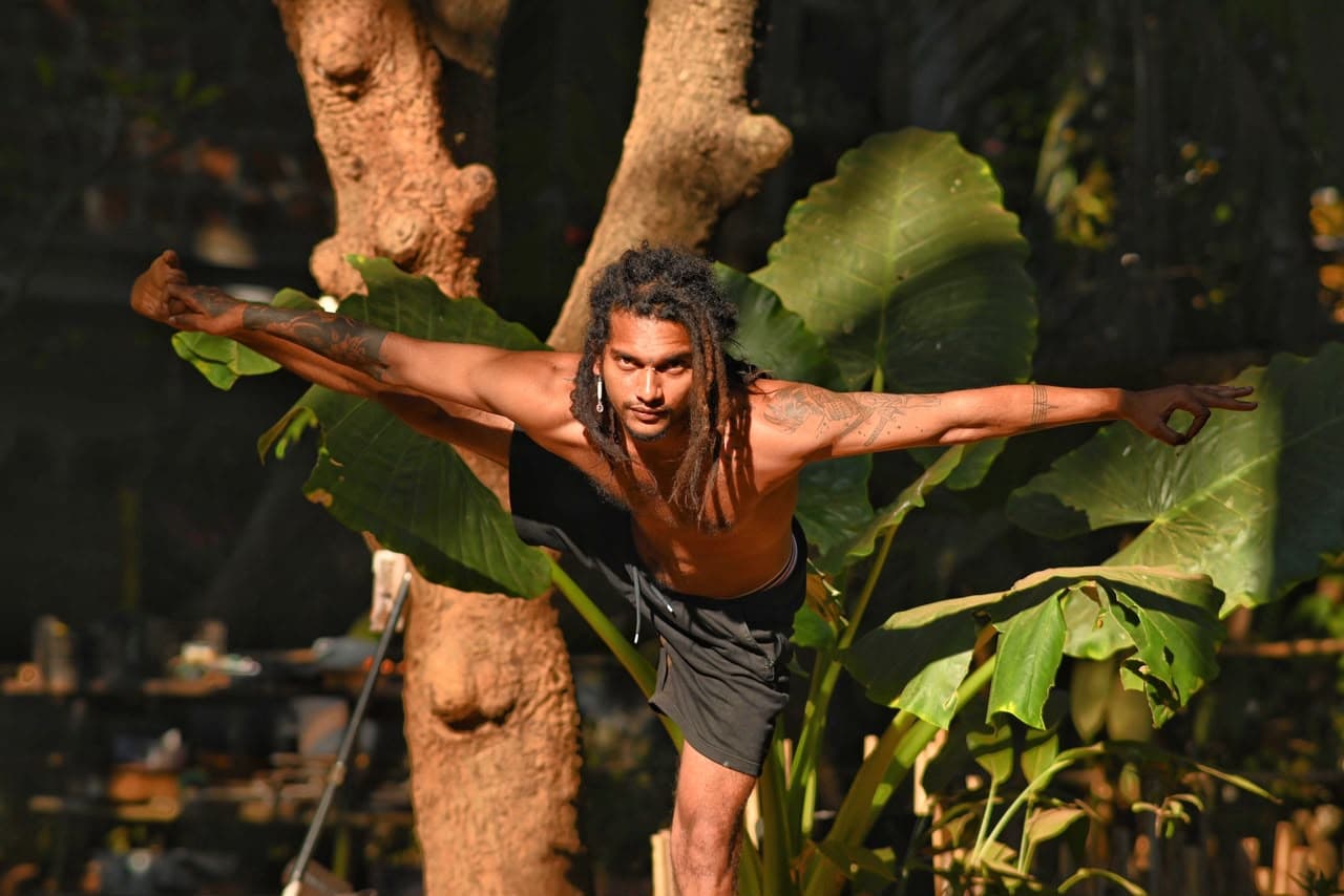 JATTAYOU balancing in a yoga pose among tropical greenery